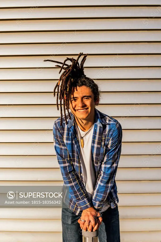 Smiling young man leaning on bollard in front of wall