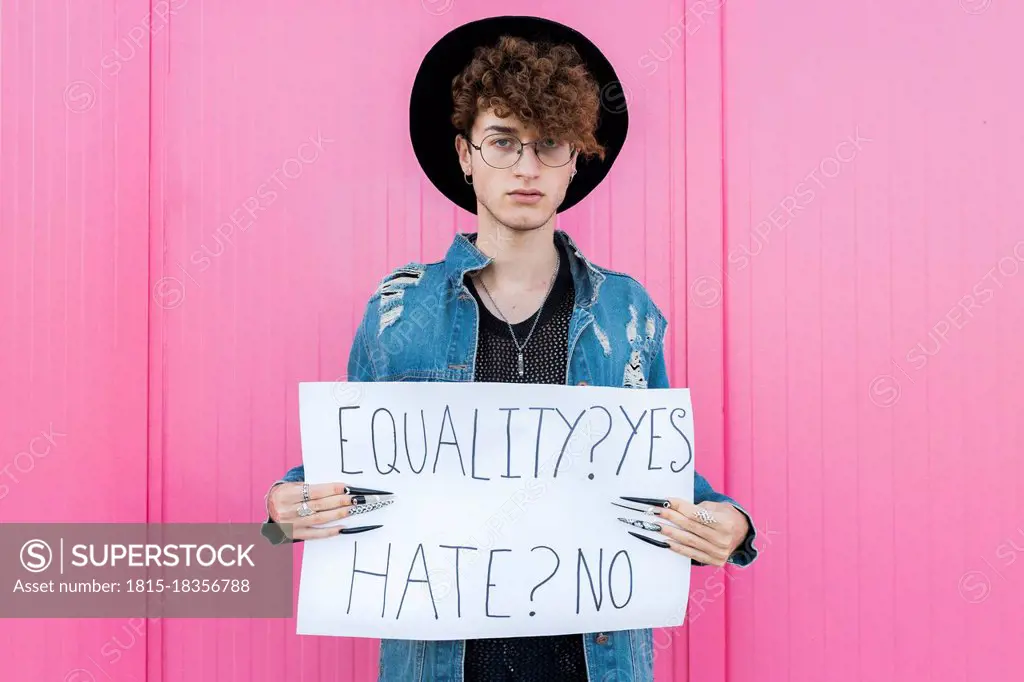 Serious gay man holding placard in front of pink wall