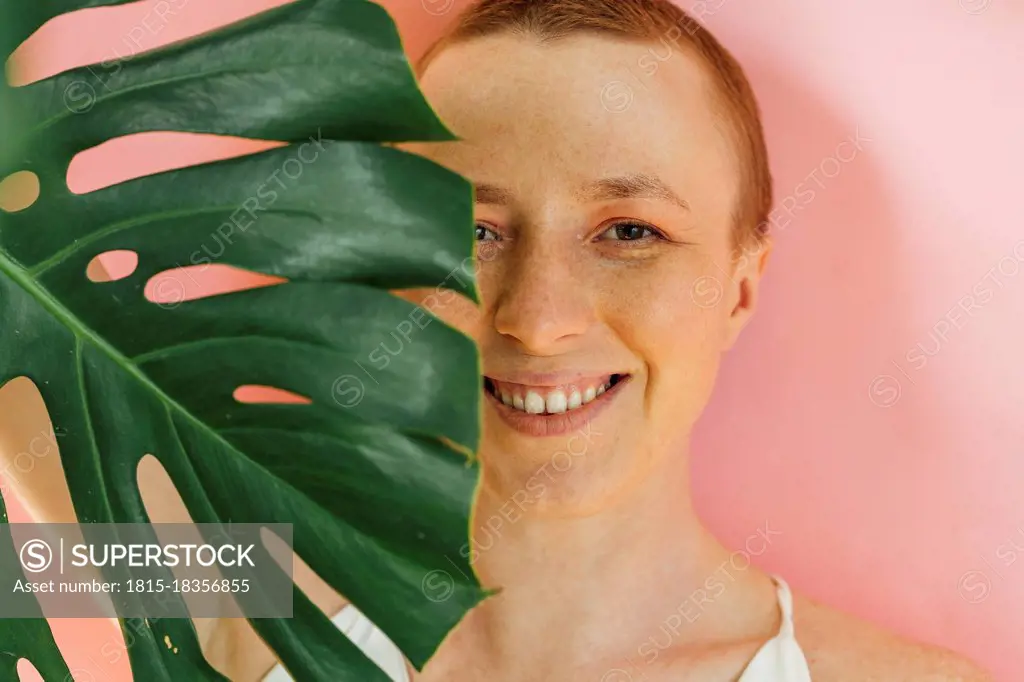 Smiling woman's half face covered with green leaf