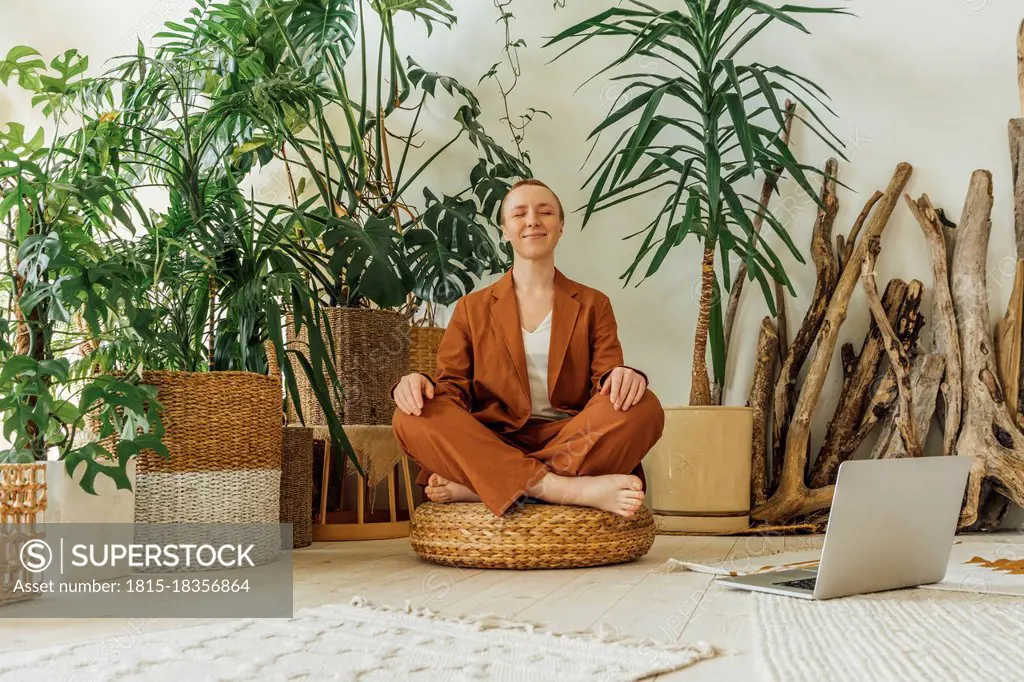 Smiling businesswoman meditating by laptop at work place