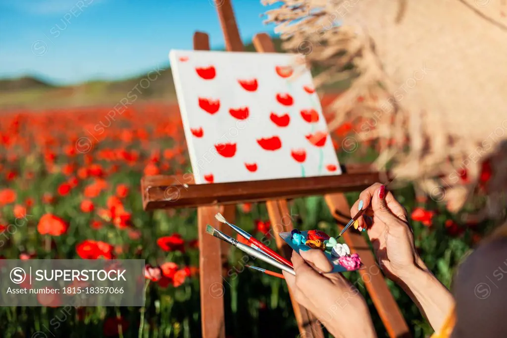 Female artist with paint on palette by canvas at poppy field