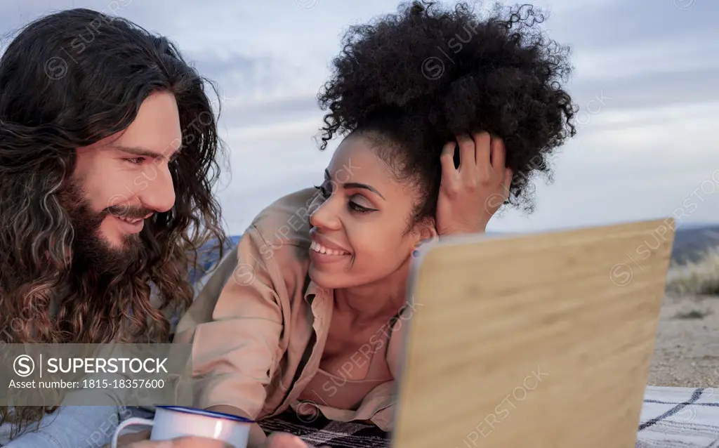 Smiling boyfriend looking at girlfriend lying by laptop