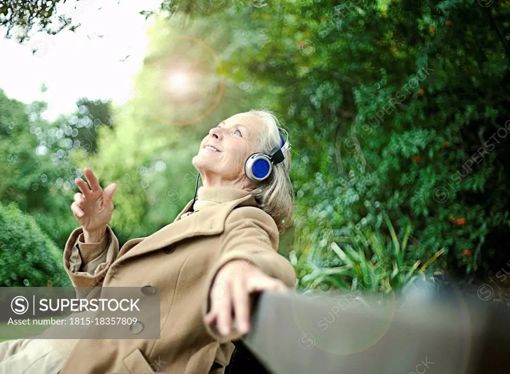 Smiling senior woman looking up while listening music on bench at public park