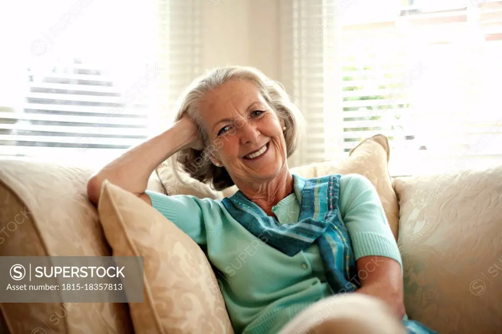 Smiling senior woman with head in hand sitting on sofa at home