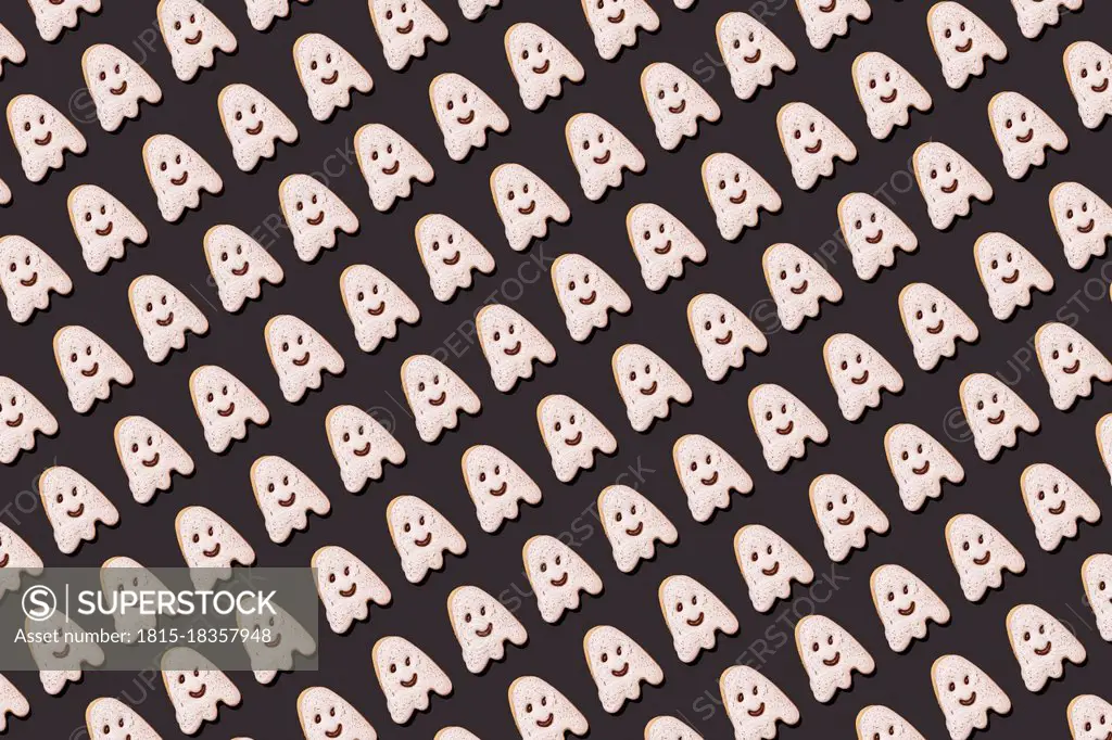 Pattern of ghost-shaped chocolate cookies flat laid against black background