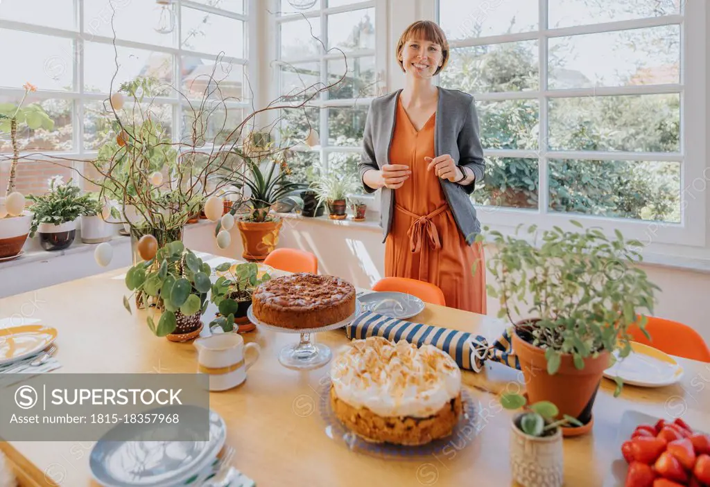 Smiling woman standing by dining table at home during Easter