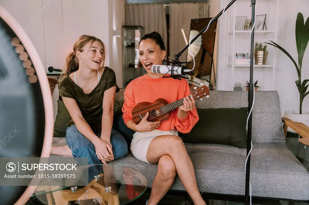 Girl sitting on sofa with female friend playing ukulele at home