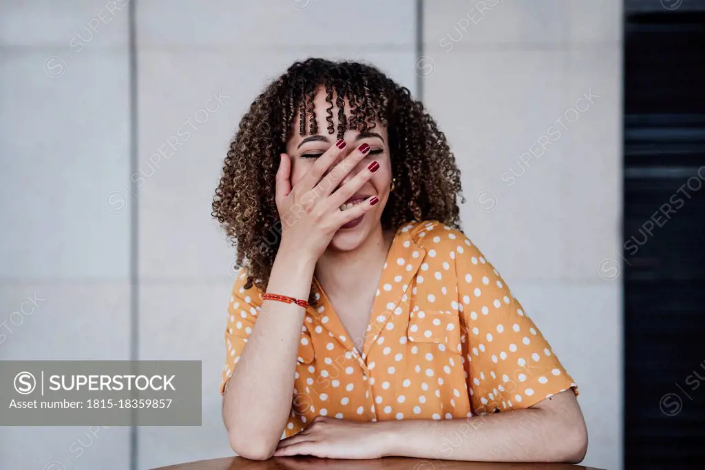 Happy woman covering mouth with hand while sitting at coffee shop