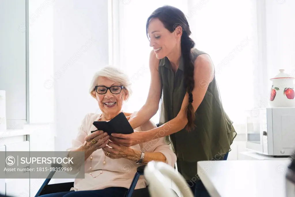 Smiling woman teaching disabled grandmother using smart phone at home