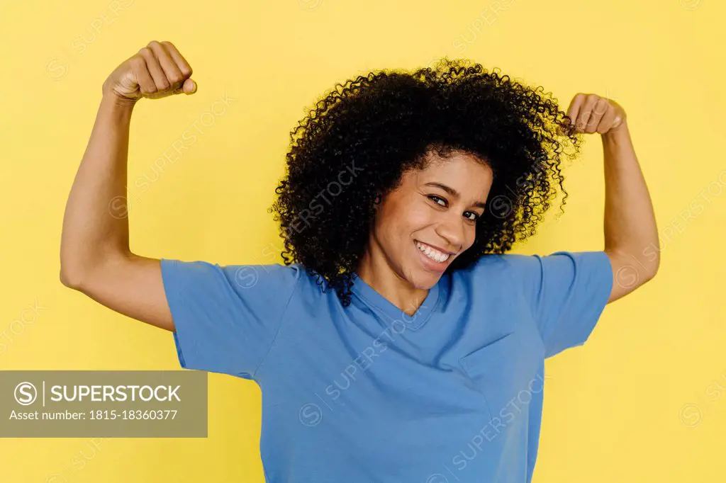 Smiling woman flexing muscles against yellow background