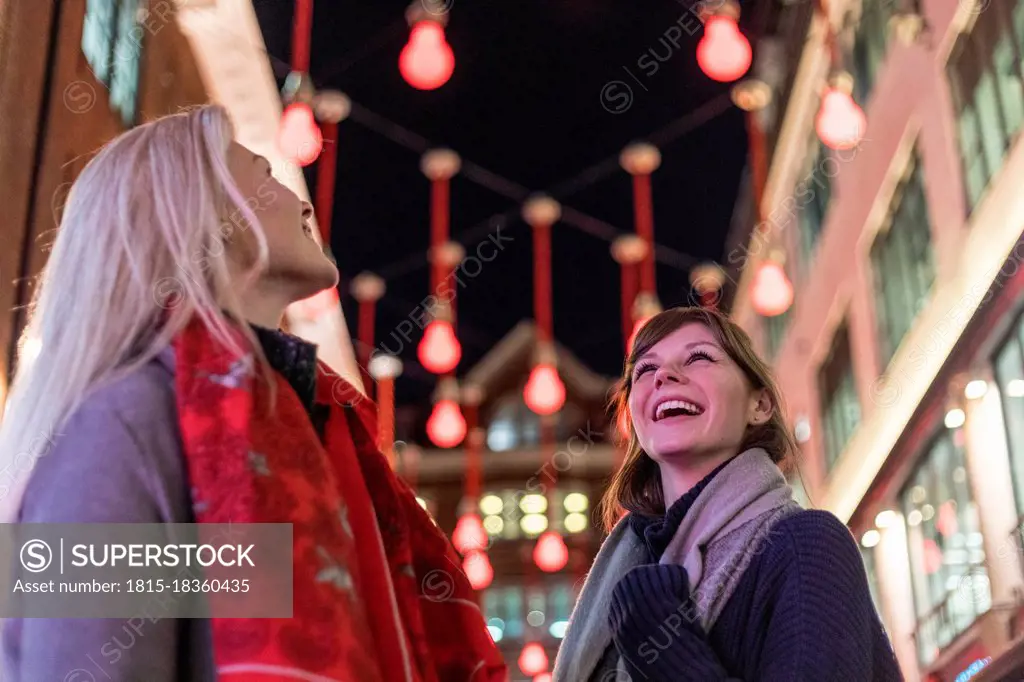 Smiling female friends looking up at Christmas lights during holiday