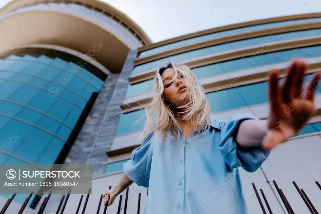 Young blond woman gesturing while standing in front of building