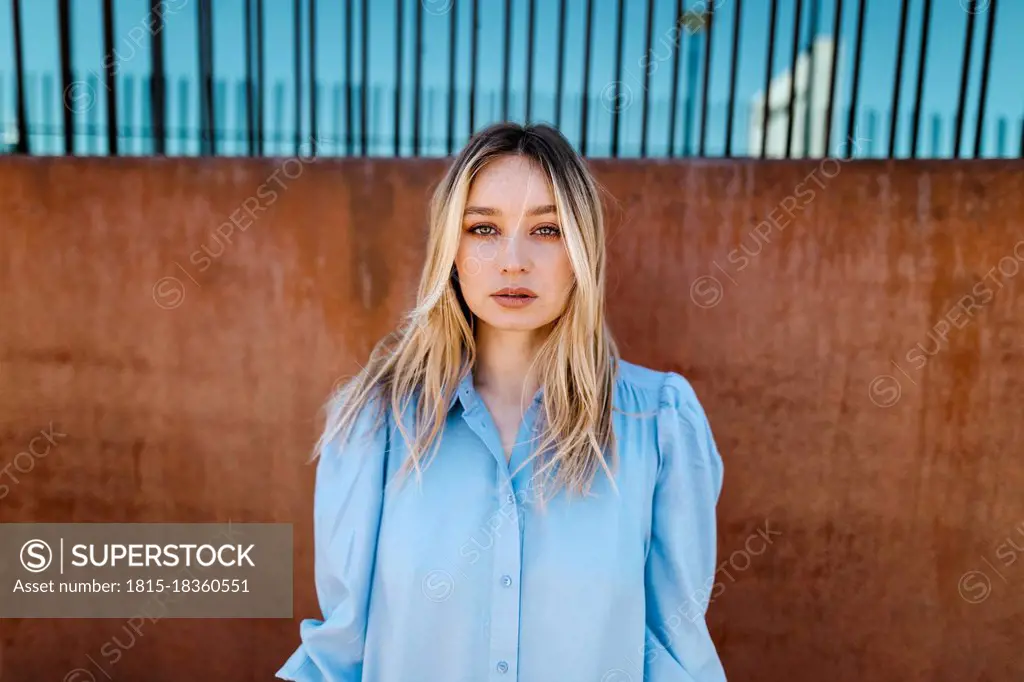 Beautiful blond young woman standing in front of brown wall