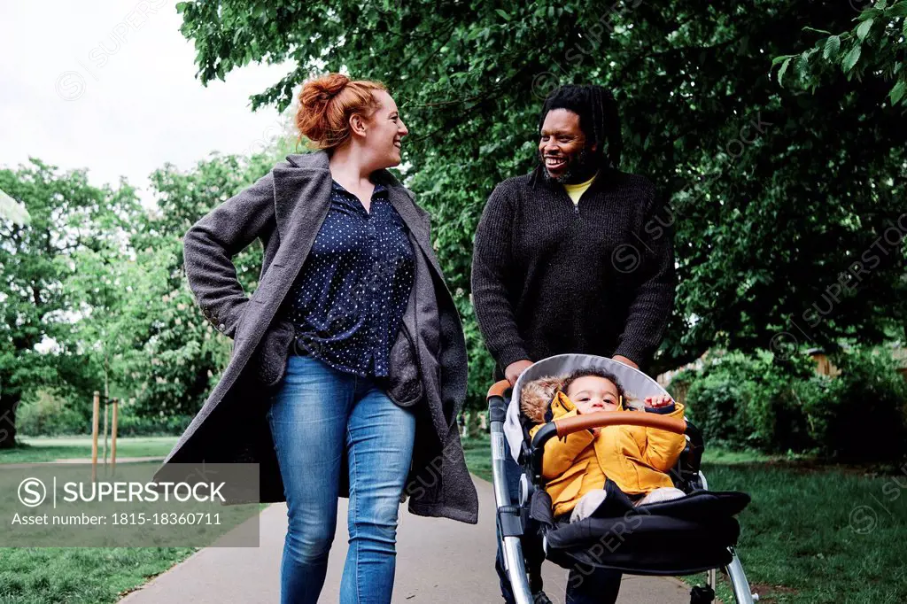 Father talking to mother while walking wheeling son in stroller at park