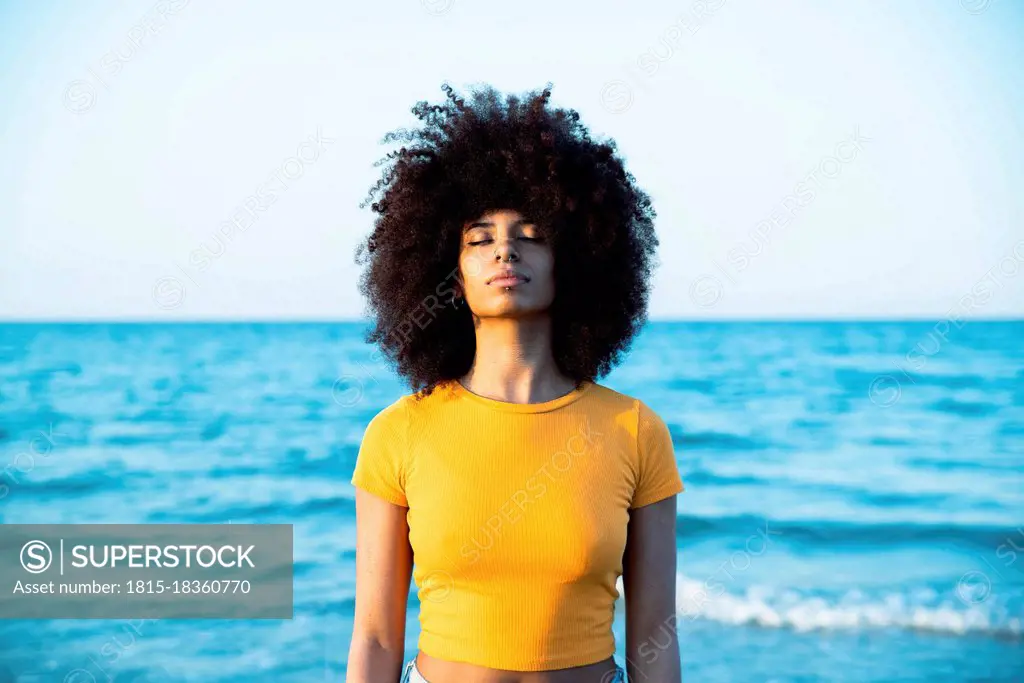 Young Afro woman with eyes closed standing at beach