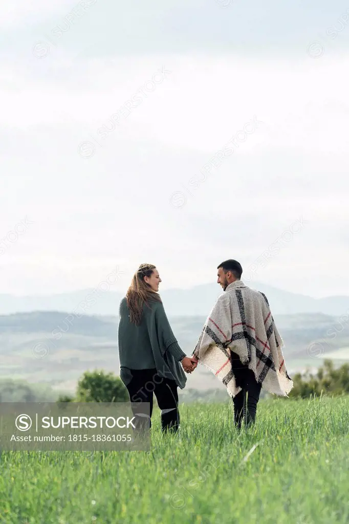 Young couple holding hands while walking together on field