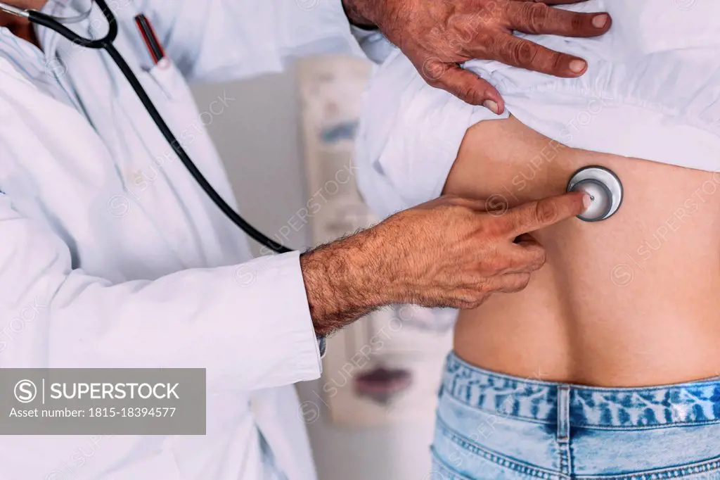 Male doctor checking female patient through stethoscope at clinic