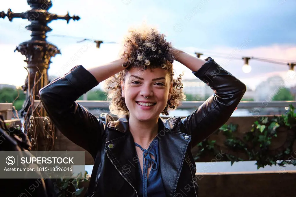 Happy beautiful young woman wearing leather jacket sitting with hand in hair