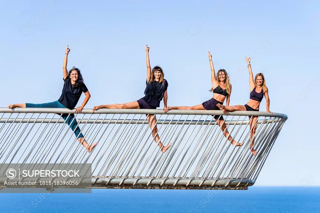 Female friends practicing acrobatic activity on railing at observation point over sea