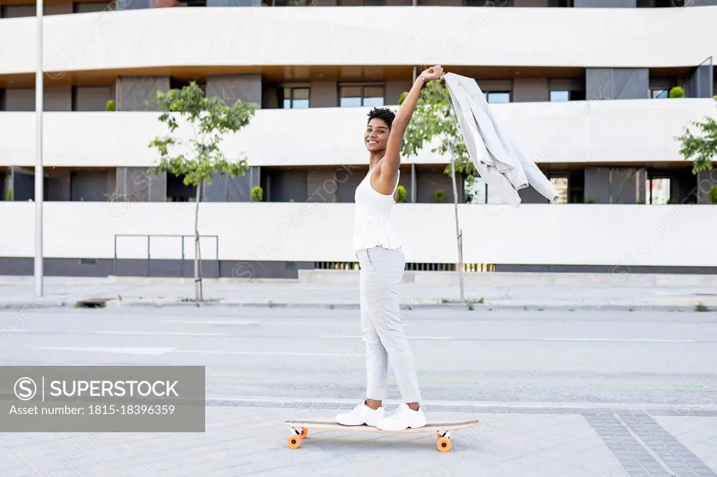 Carefree businesswoman holding blazer while skateboarding in city