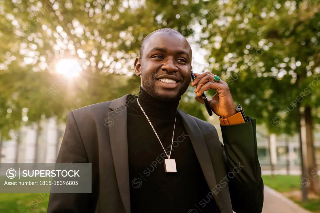 Fashionable man smiling while talking on smart phone at park