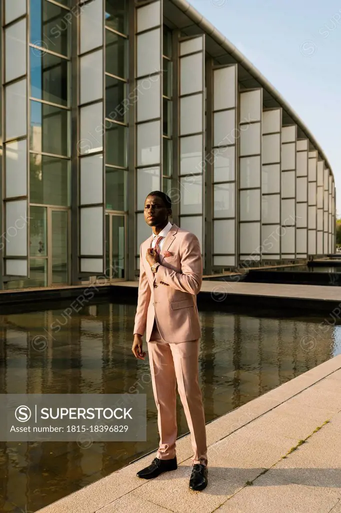 Elegant man wearing suit standing on footpath by pond