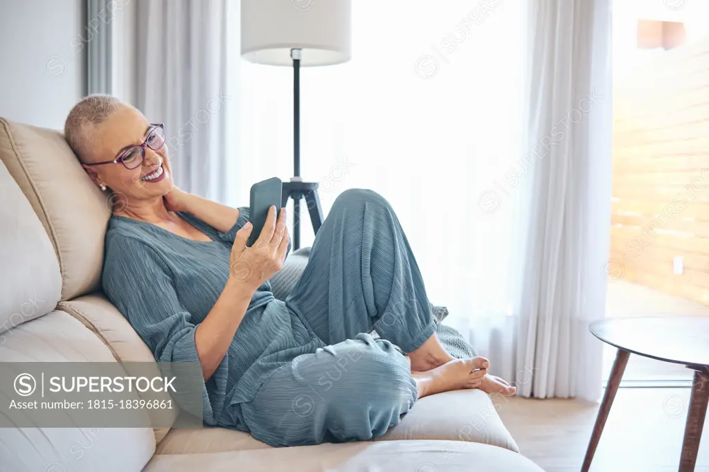 Smiling mature woman using smart phone while sitting on sofa at home