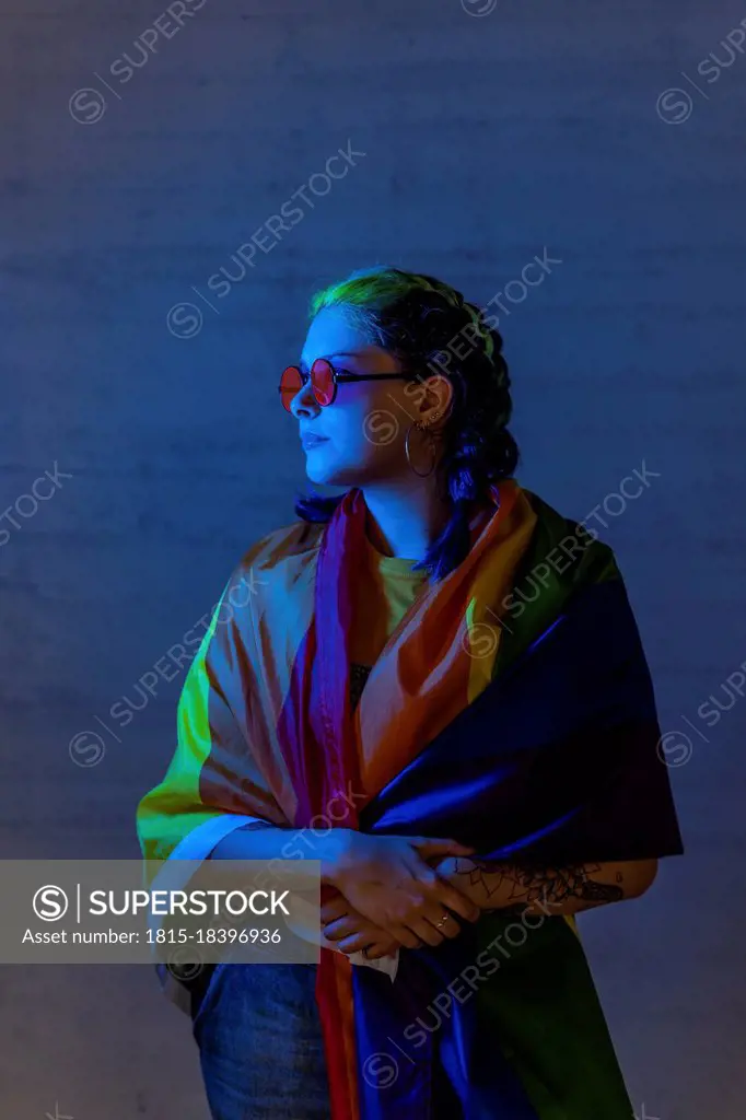 Hipster woman looking away while covering self with rainbow flag