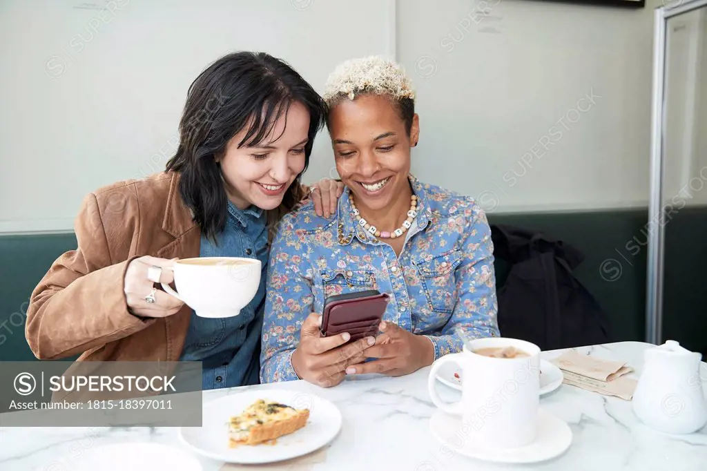 Happy lesbian couple sharing smart phone while sitting in cafe