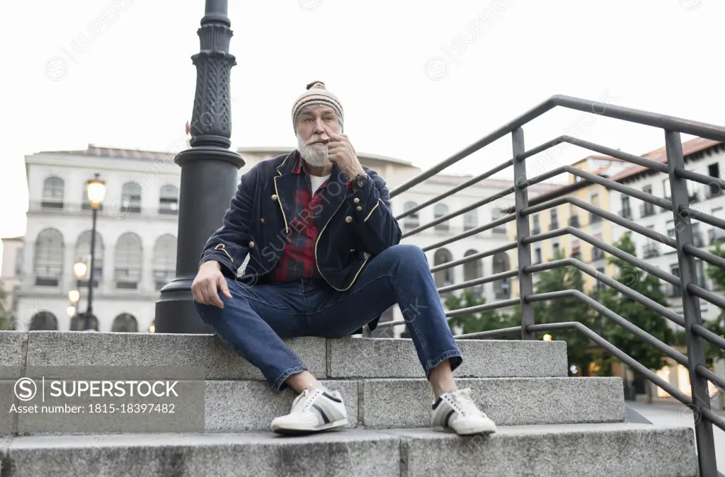 Mature man looking away while smoking pipe on steps