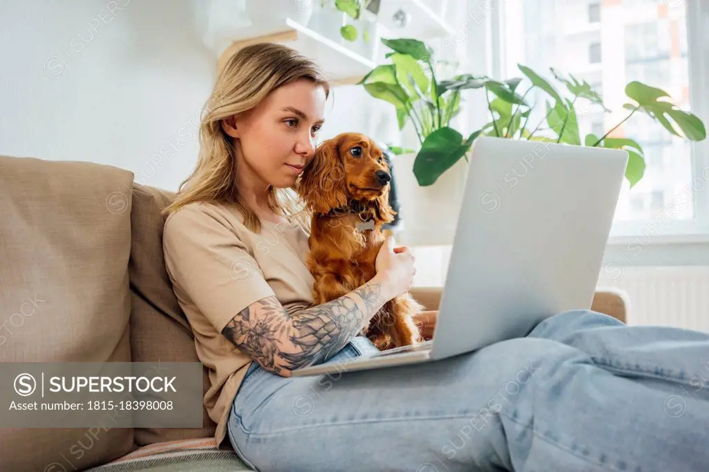 Female professional sitting with dog while working on laptop at home