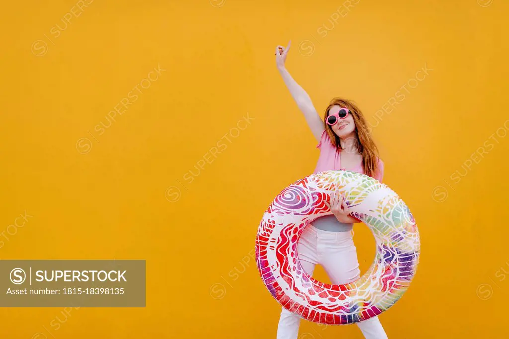 Carefree woman with hand raised holding inflatable ring