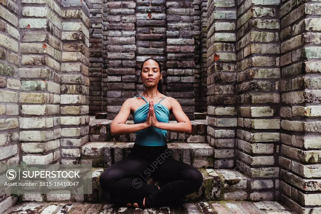 Young woman meditating with hands clasped in stone structure