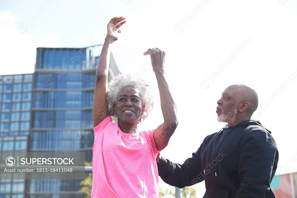 Man helping woman exercising with hands raised at park