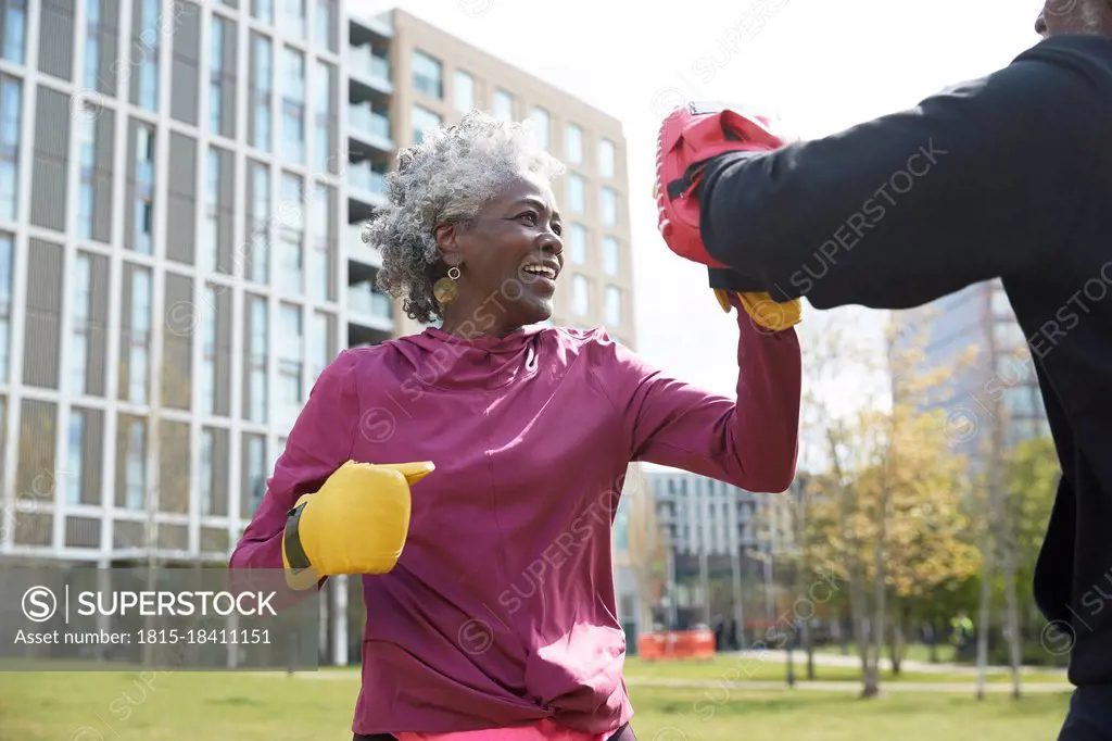 Smiling woman practicing boxing with man at park on sunny day