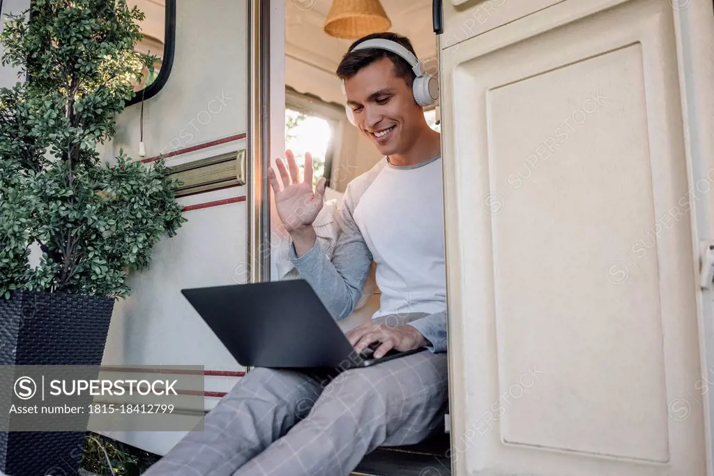 Smiling male freelancer waving hand during video call through laptop