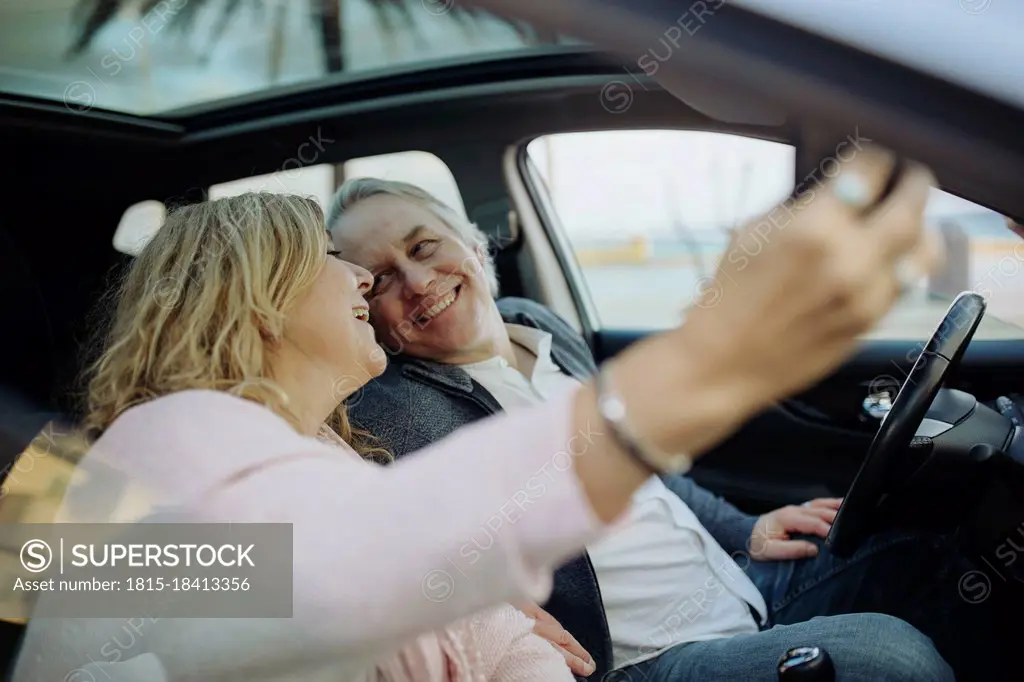 Happy mature couple looking at each other while taking selfie sitting in car