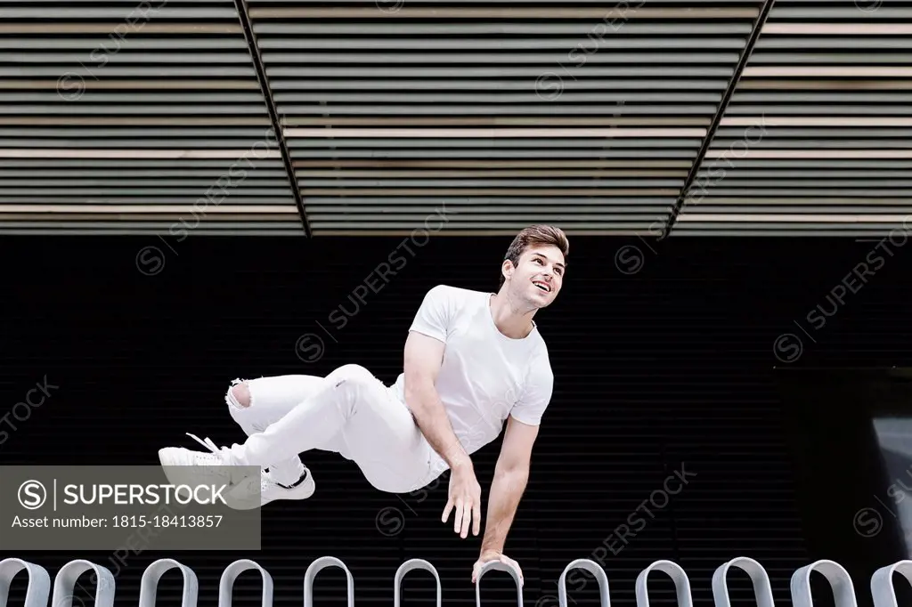 Young man looking away while jumping over railing