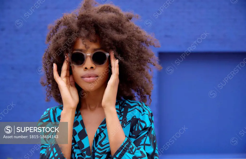 Afro woman wearing sunglasses in front of blue wall