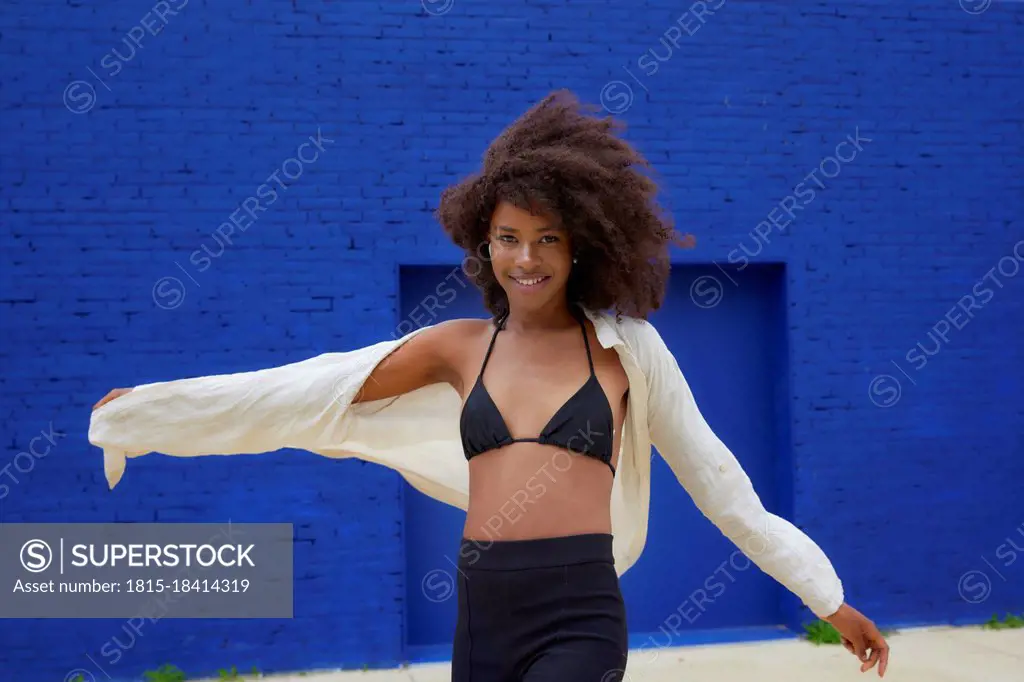 Smiling young woman dancing in front of blue wall