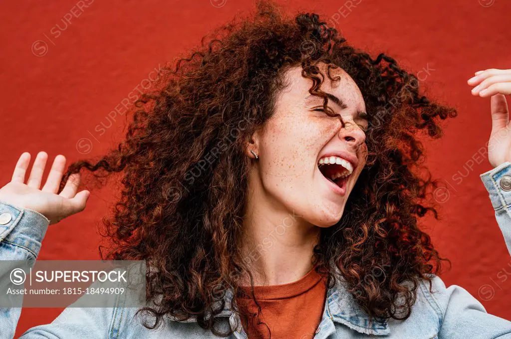 Cheerful young woman with curly hair singing in front of red wall