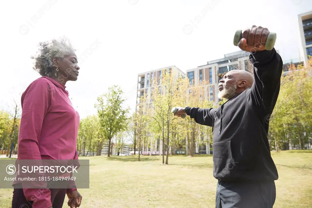 Senior woman looking at man exercising with dumbbells in public park