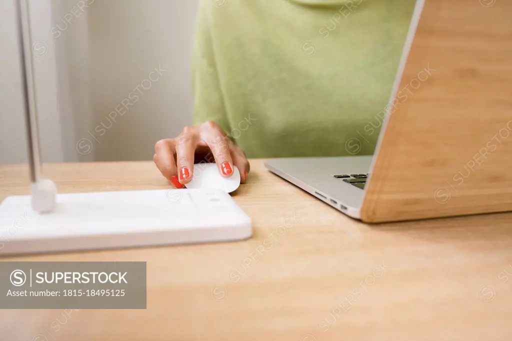 Woman using computer mouse while working on laptop