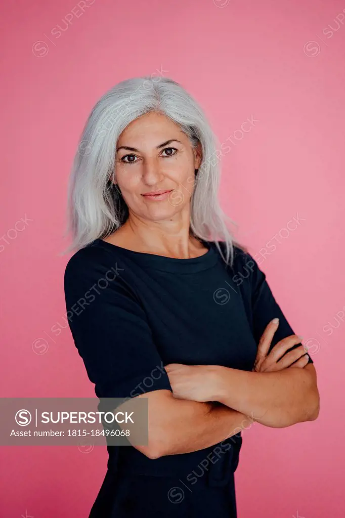 Female professional with arms crossed standing by pink background