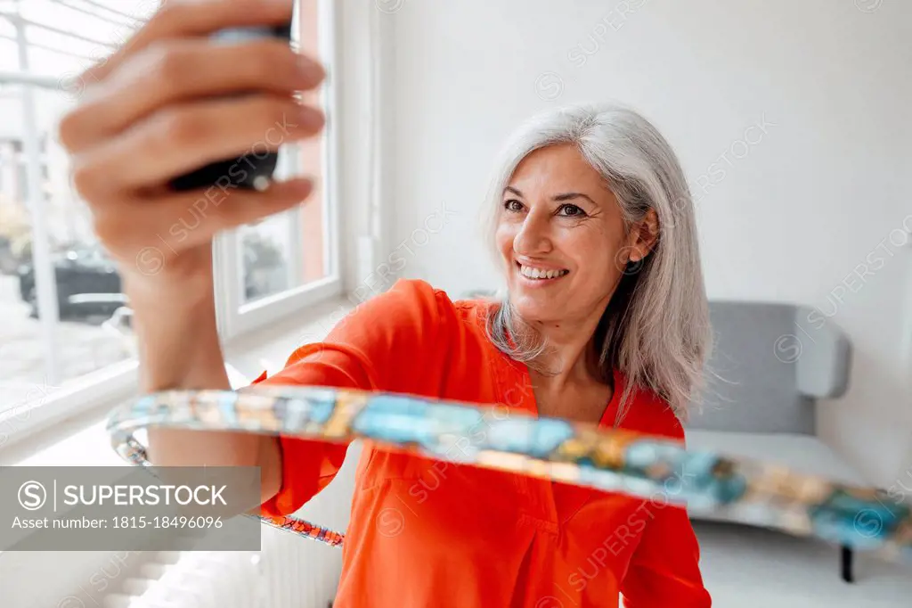 Smiling businesswoman taking selfie through smart phone while practicing with hula hoop at office