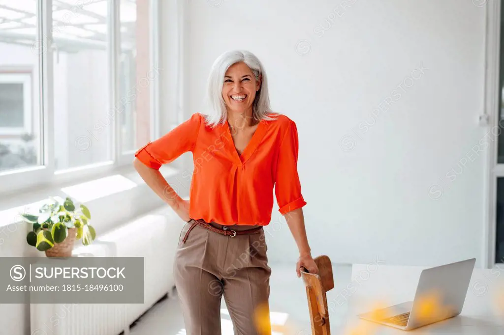 Smiling businesswoman with hand on hip standing at desk in office