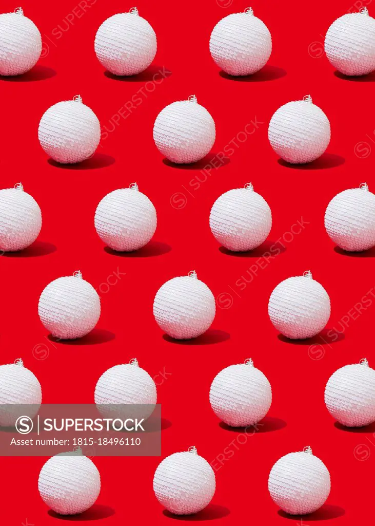 Pattern of white-colored Christmas ornaments flat laid against vibrant red background