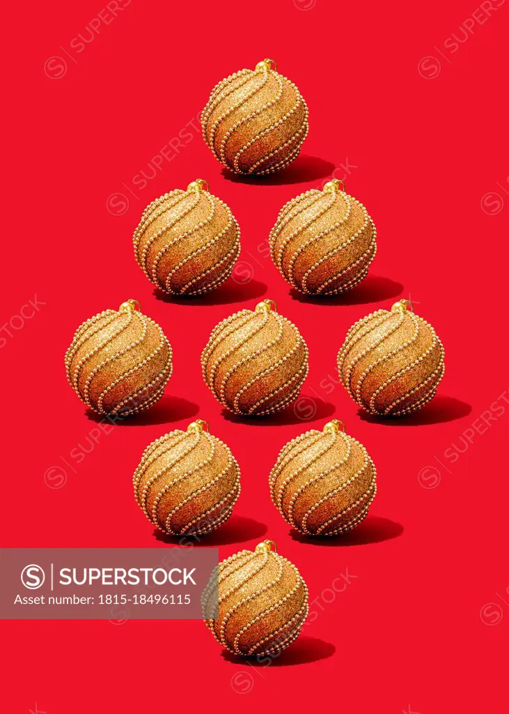 Studio shot of gold-colored Christmas ornaments flat laid against vibrant red background