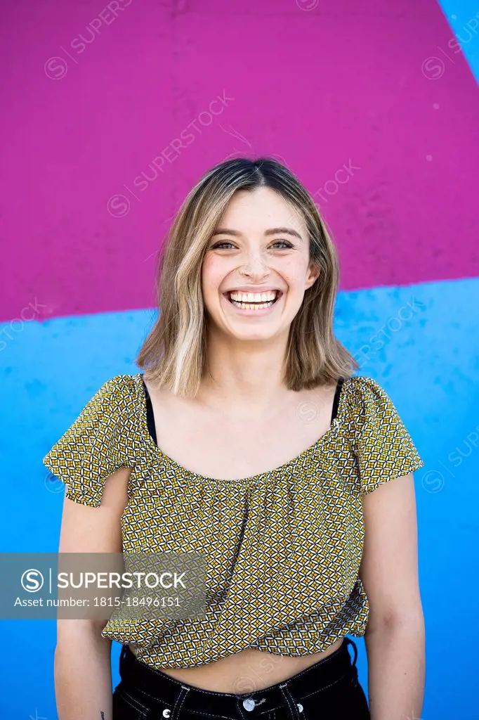 Cheerful young woman smiling in front of colorful wall