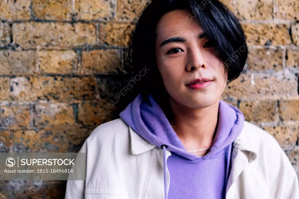 Young man wearing purple hooded shirt in front of brick wall